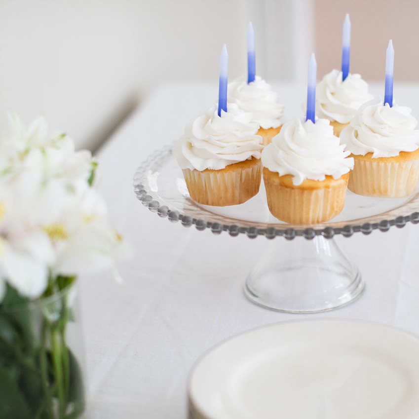 White cupcakes with blue ombre candles on a platter