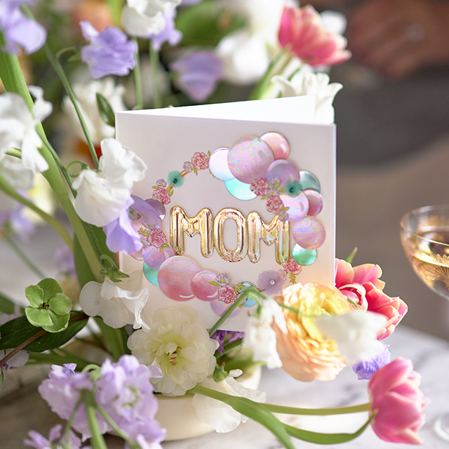 Mother's Day card among flowers that reads MOM.