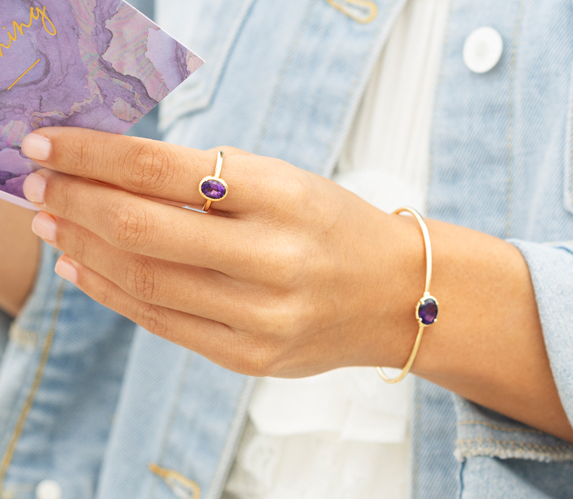 A hand holding a card wearing rings and a bracelet.