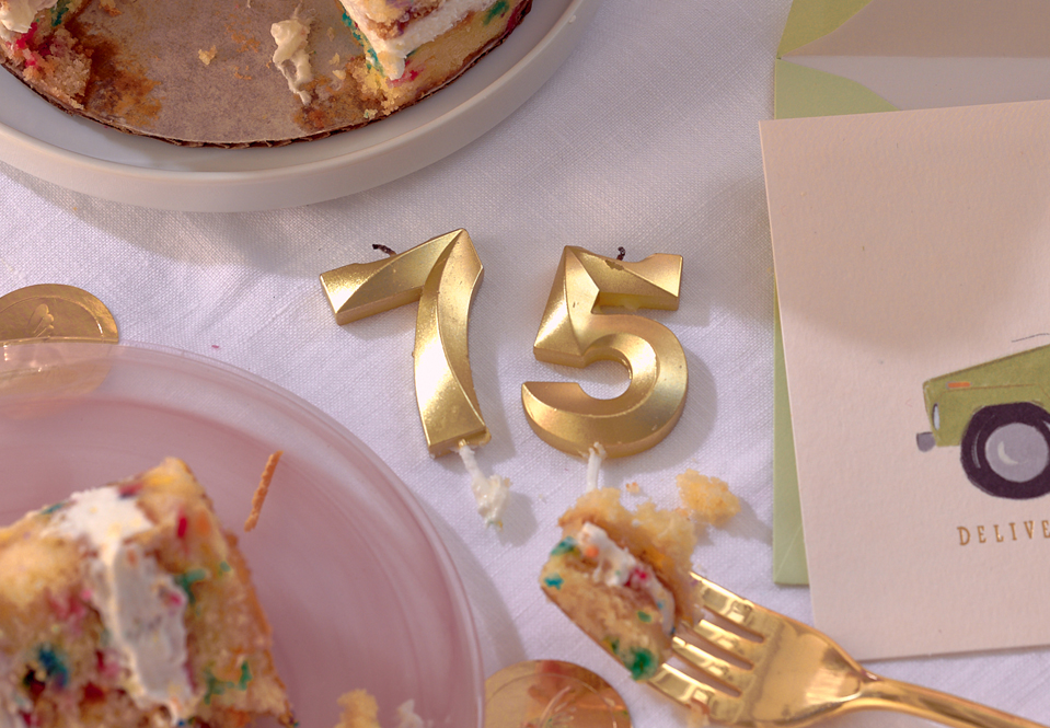 Gold number 75 candles on a table with a greeting card and gold fork