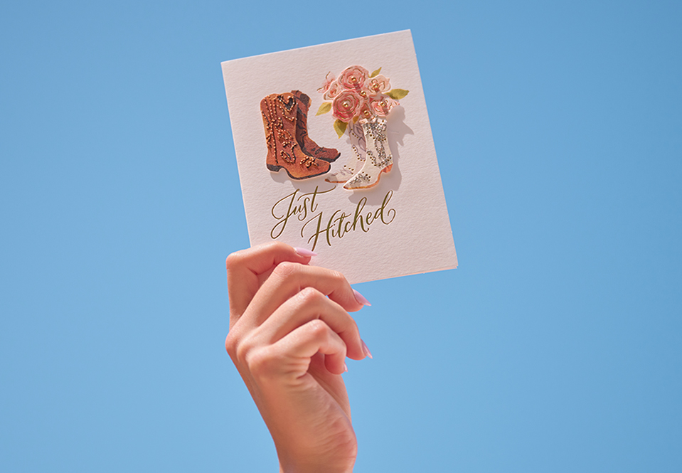 A hand holding a wedding card in the sky