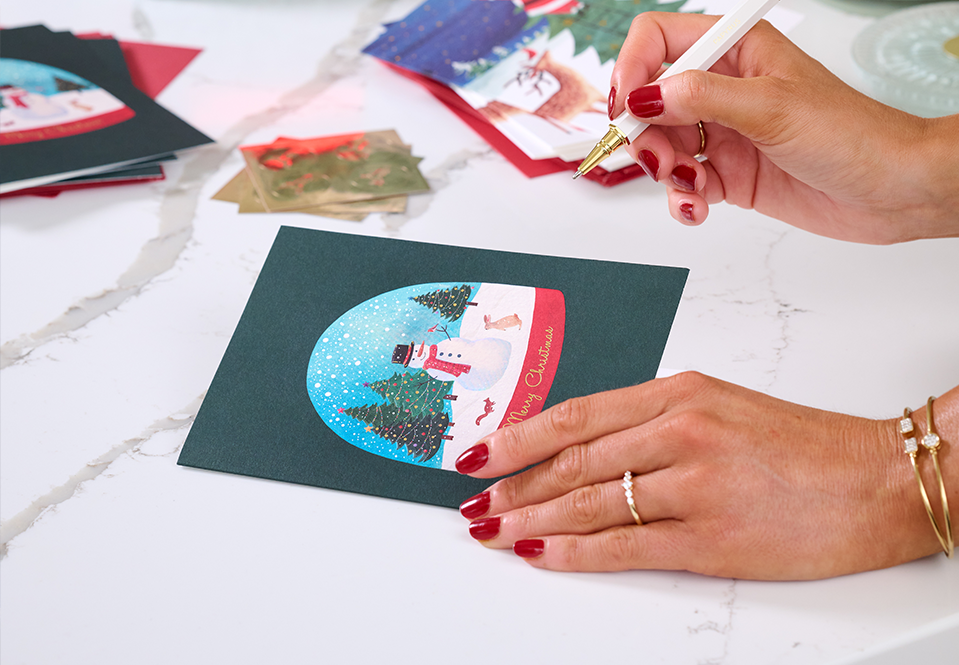Person writing in a Christmas card with a Papyrus pen.