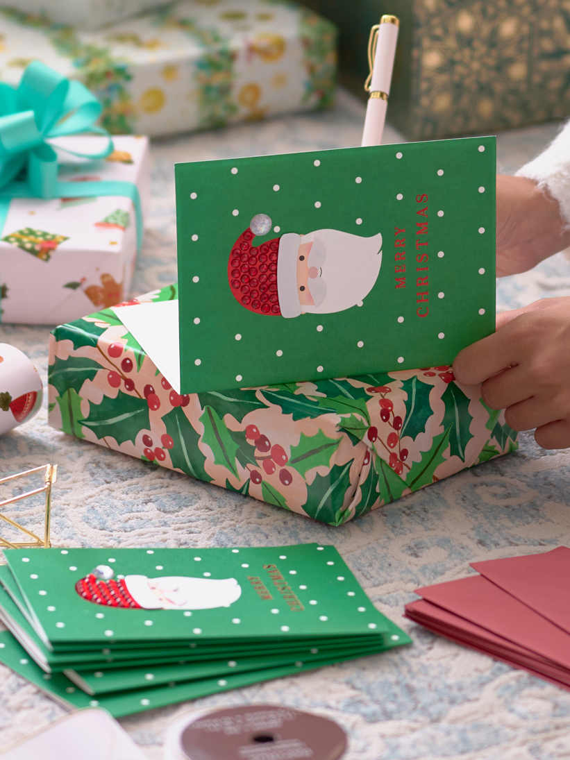 Person writing holiday cards on the floor with gifts around.