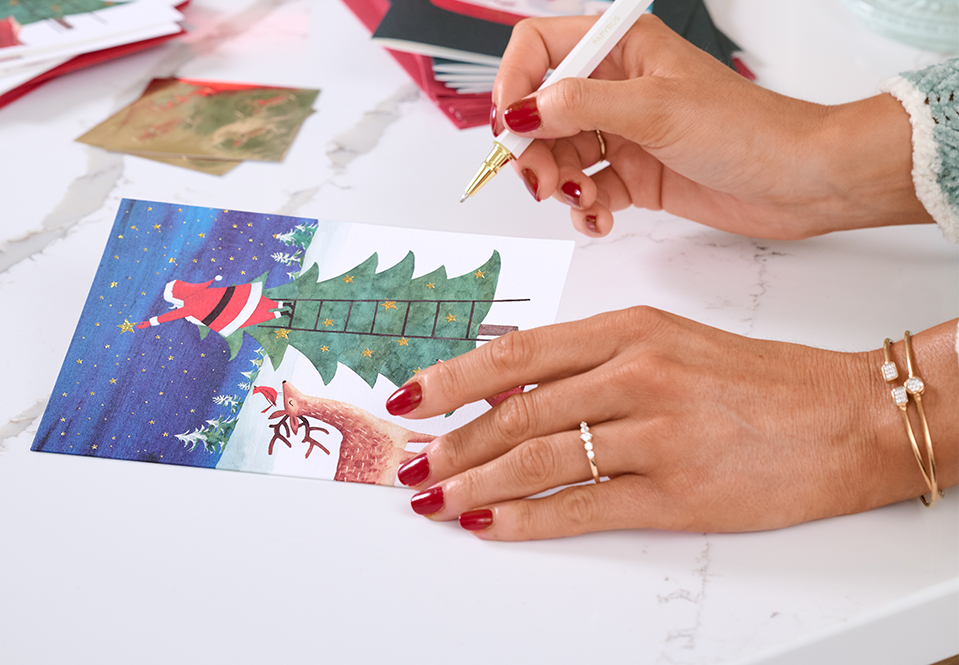 Person writing in a Christmas card with a Papyrus pen.