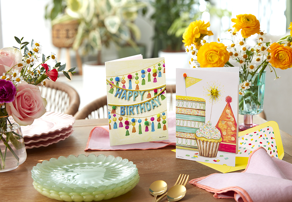 Two birthday cards standing on a table with flowers