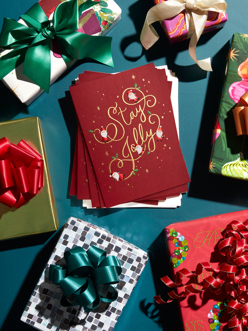 Stay Jolly holiday boxed cards on a table with wrapped Christmas gifts.